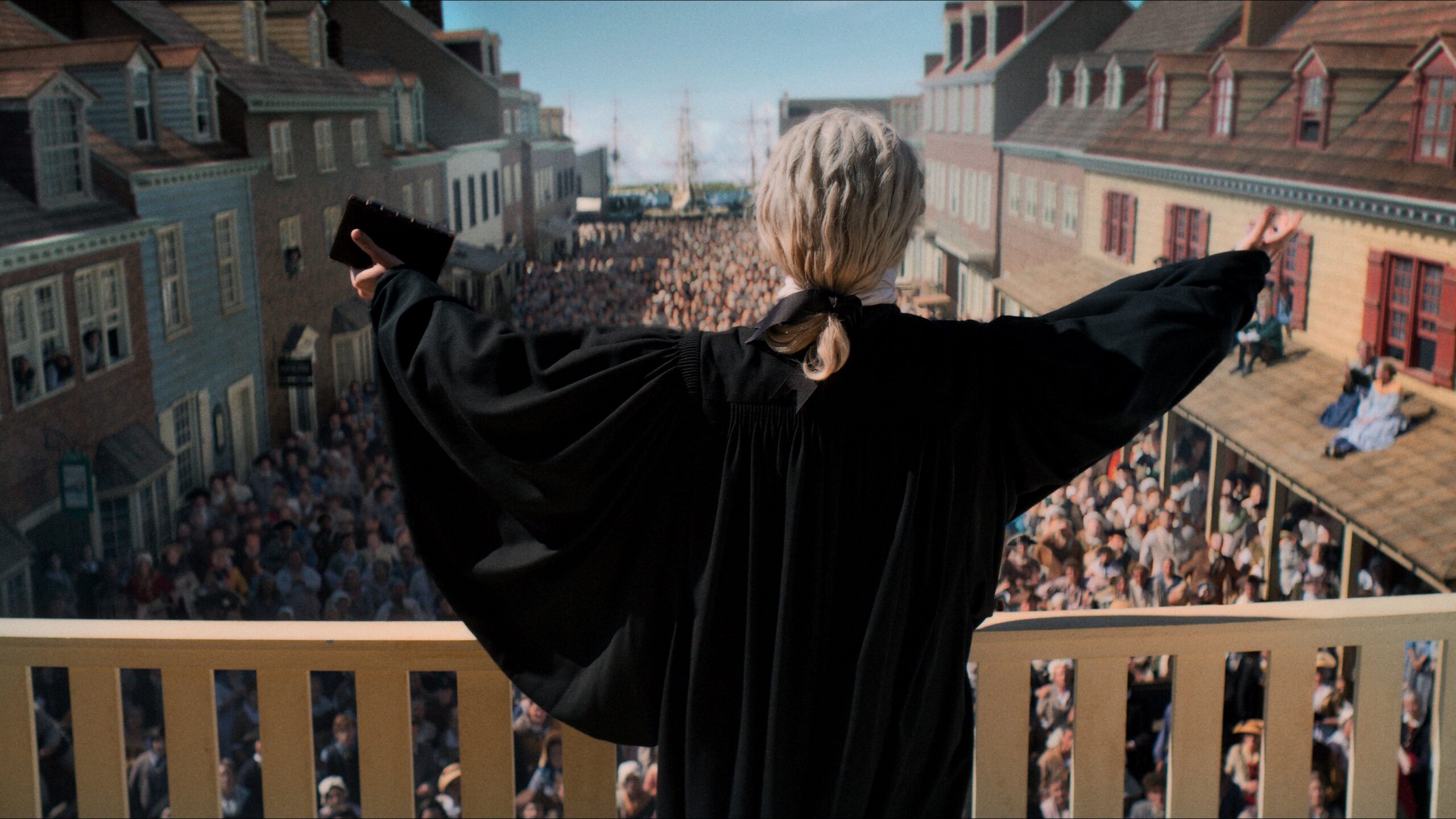 George Whitefield holds a Bible and extends his arms from a balcony above a street filled with listeners in A Great Awakening.